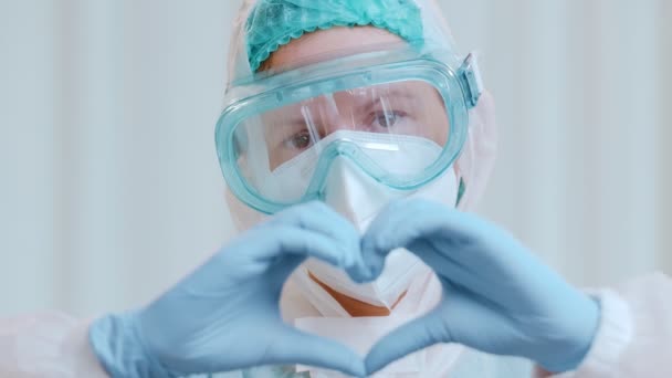 Il primo piano di un medico in una tuta protettiva mostra un cuore piegato dalle mani. — Video Stock