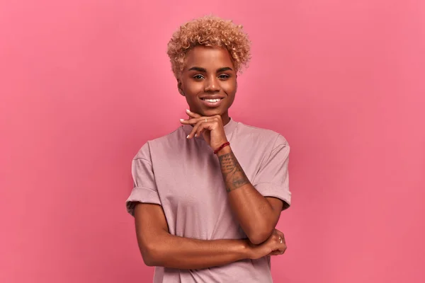 Pembe arka planda poz veren günlük tişörtlü Afro-Amerikan kadın..