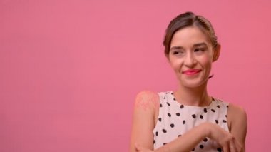 Gülümseyen kadın pembe arka planda duruyor ve avuçlarını boş alana gösteriyor..
