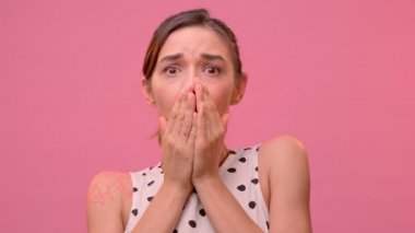 Çekici bir genç kadın pembe bir arka planda sersemlemiş ve şok olmuş görünüyor..