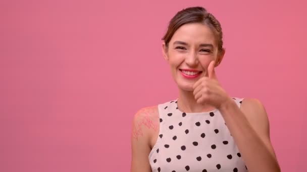 Ung kaukasisk kvinna höja tummen upp på en rosa bakgrund. — Stockvideo