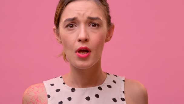 Close-up portret van een boos vrouwtje schreeuwen WTF op een roze achtergrond. — Stockvideo