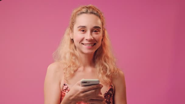 幸せな女の子を保持しています携帯電話と作る良いジェスチャーオンピンクの背景. — ストック動画