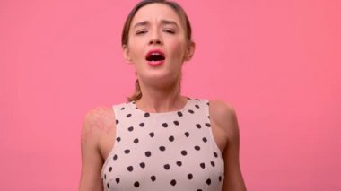 Genç bir kız soluk pembe bir arka planda stüdyoda hapşırır..