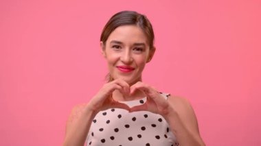Güzel kız ellerini pembe arka planda bir kalp şeklinde gösterir..