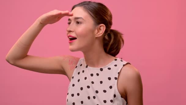 Mujer buscando alegre y ansiosamente a alguien sobre un fondo de una pared rosa. — Vídeos de Stock