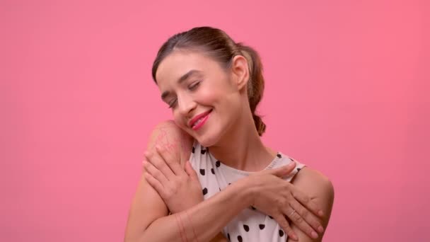 Frau mit geschlossenen Augen umarmt sich vor rosa Wand. — Stockvideo