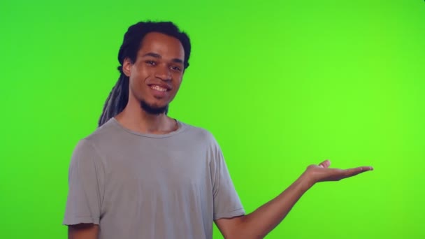 Allvarligt strikt ung man presenterar kopia utrymme på grön bakgrund — Stockvideo