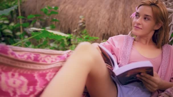 Mujer pelirroja joven vestida de Kimono rosa, libro de lectura en hamaca colorida — Vídeo de stock