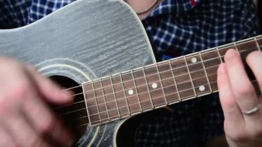 Mavi Kareli gömlekli bir adam bir yakın çekim gitar çalıyor
