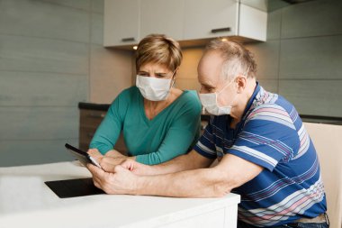 Tıbbi maske takan ve evde tablet kullanan son sınıf çifti. Karantinaya alındı. Sağlık konsepti. Corona Virüsü. Ürün sırası çevrimiçi