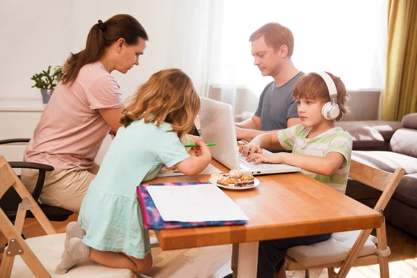Anne, baba ve iki çocuk hep birlikte masada oturuyor. Çocuklar evde onlay öğrenirler. Çocuklarla evde çalışmak. Karantina. Merkez Ofis.