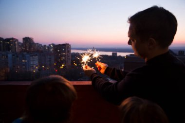 Aile babası ve iki çocuk, gün batımında evin balkonunda maytaplı maytaplarla. Corona Virüsü. Evde dikiliyorum. Chelter yerinde. Karantina sona erdi. ev tatili