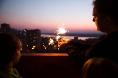 Aile babası ve iki çocuk, gün batımında evin balkonunda maytaplı maytaplarla. Corona Virüsü. Evde dikiliyorum. Chelter yerinde. Karantina sona erdi. ev tatili