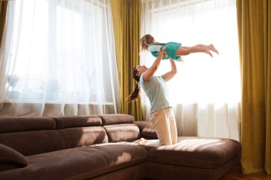 Anne ve küçük kızı evde birlikte vakit geçiriyorlar. Mutlu anne, küçük tatlı kızını uçakla oynarken kaldırıyor. Evde kal..
