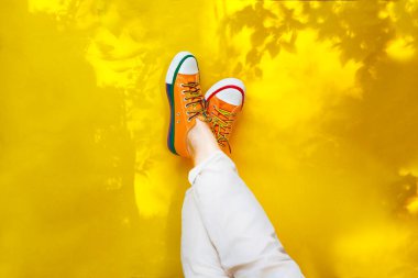 Sarı spor ayakkabılı kadın bacakları, sarı arka planda, ağaçların gölgesinde. Karantina sona erdi. Merhaba yaz. Yaz zamanı.