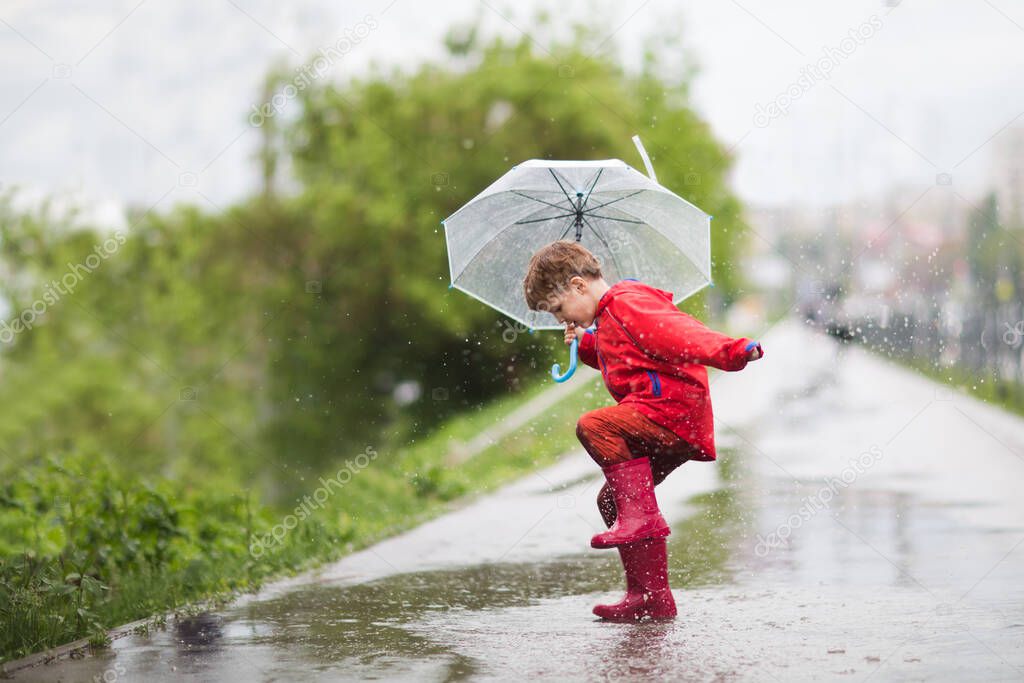 little child boy with an umbrella playing out in the rain in the summer outdoors