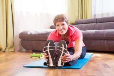 Aktif kıdemli kadın evde sağlıklı idman yapıyor. Uzaktan antrenman. Evden antrenman yapıyorum. Ev yapımı spor salonu. ev fitness, aktif giyim.