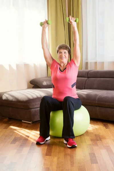 Cheerful senior lady exercising with dumbbells in the home.  Remote Workouts. Working out from home.  home-based gym. home fitness, activewear.