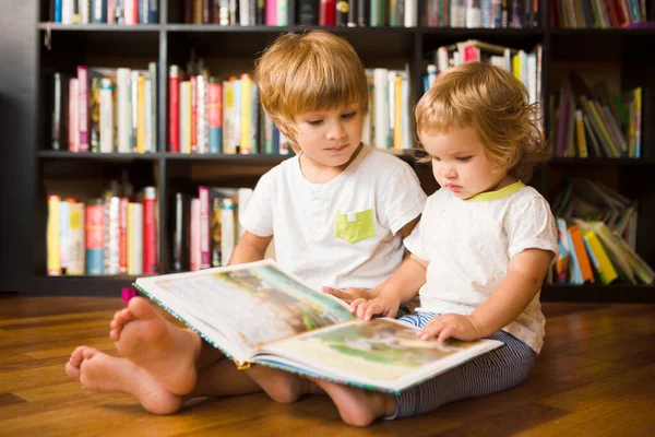 Şirin çocuk ve küçük kız kardeşi evde kitaplığın yanında birlikte kitap okuyorlar. Evde eğitim, uzak öğrenim 