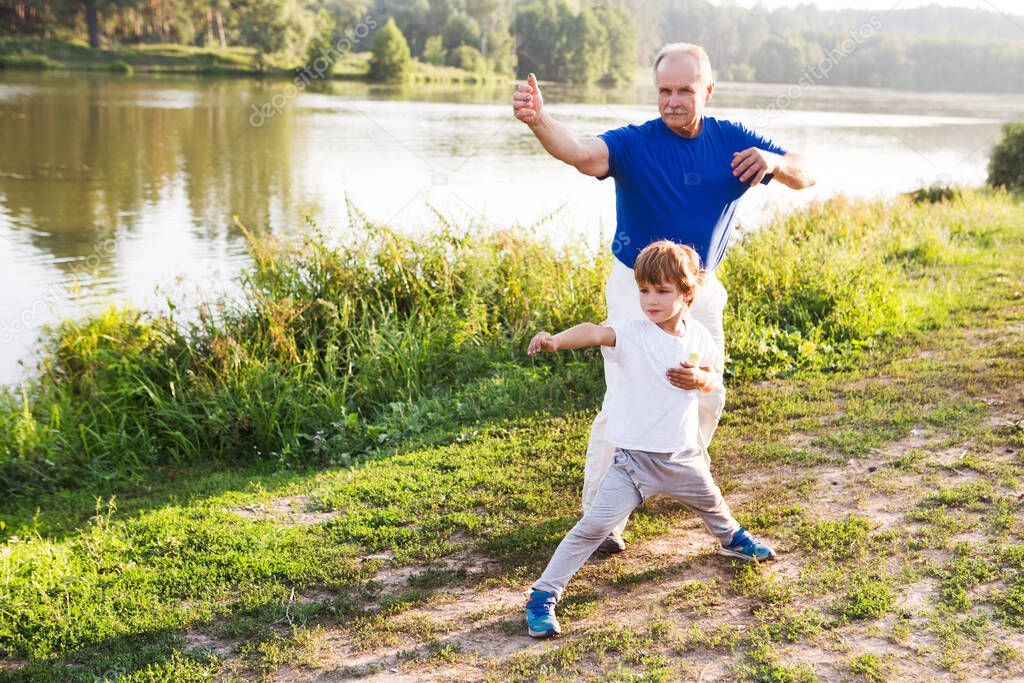 Grandfather and little grandson  practice Tai Chi Chuan outdoors.  Chinese management skill Qi's energy.