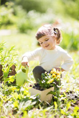 Bahçede sulama tenekesiyle çiçek sulayan tatlı küçük bir kız..