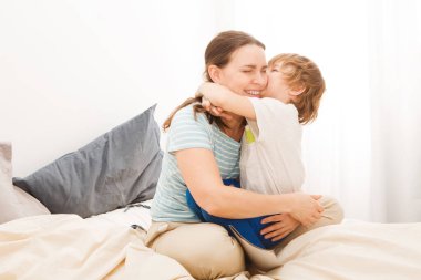 Küçük oğlum annesine sarılıyor ve onu öpüyor ve hafta sonu birlikte yatakta oynuyorlar, tembel bir sabah. Anneler Günü..