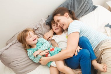 Anne ve küçük çocukları hafta sonu birlikte yatakta oynuyorlar, tembel bir sabah..