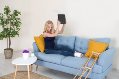 Kırık bacaklı öfkeli genç kadın dizüstü bilgisayarını parçalamak üzere. 