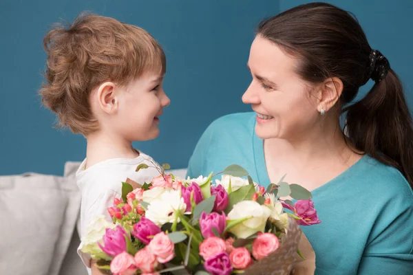 Милый Маленький Ребенок Обнимает Целует Свою Мать Предлагает Цветы Синем — стоковое фото