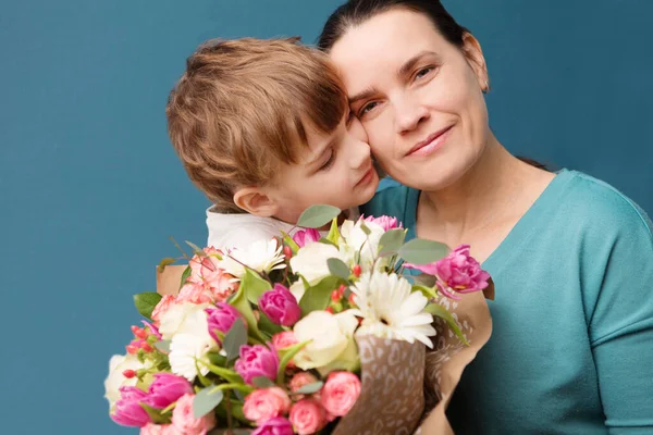 Bonito Criança Abraçando Beijando Sua Mãe Oferecendo Flores Fundo Azul — Fotografia de Stock
