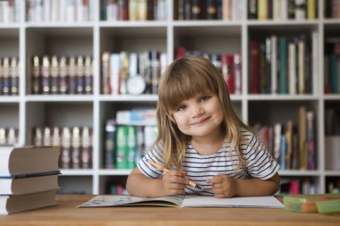 Çocuk evde ders alıyor. Çocuk evde ders çalışıyor. Karantinaya alındı. Corona Virüsü. Liseli kız evde online ders çalışıyor. Evde eğitim, uzak öğrenim. Okul çocuğu arka planda bir kitaplık ile masada çizim yapıyor.