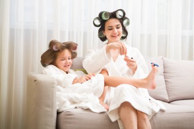 Saçlarında bigudiler olan anne ve kız evde manikür ve pedikür yapıyorlar. Saçlarında bigudiler var. Birlikte güzel vakit geçiriyoruz. Chelter yerinde. ev konsepti