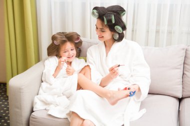 Saçlarında bigudiler olan anne ve kız evde manikür ve pedikür yapıyorlar. Saçlarında bigudiler var. Birlikte güzel vakit geçiriyoruz. Chelter yerinde. ev konsepti