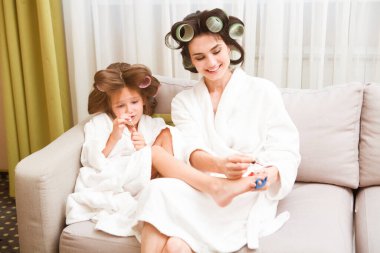 Saçlarında bigudiler olan anne ve kız evde manikür ve pedikür yapıyorlar. Saçlarında bigudiler var. Birlikte güzel vakit geçiriyoruz. Chelter yerinde. ev konsepti