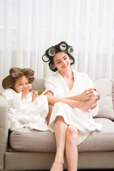 Mom and daughter  in white bathrobes with curlers in their hair Make manicure and pedicure at home. They have curlers in their hair. cheerful time together. chelter in place. stay home concept