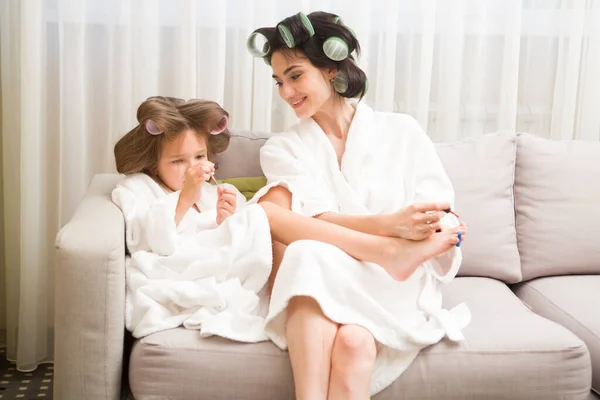 Mom and daughter  in white bathrobes with curlers in their hair Make manicure and pedicure at home. They have curlers in their hair. cheerful time together. chelter in place. stay home concept