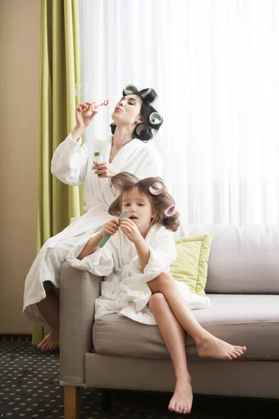 Mom and daughter  in white bathrobes with curlers in their hair Make manicure and pedicure at home. They have curlers in their hair. cheerful time together. chelter in place. stay home concept