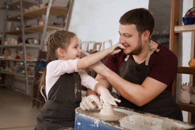 Çömlek işinde öğretmen ve kız öğrenci. Baba ve küçük kız yerlerinde eğleniyorlar.