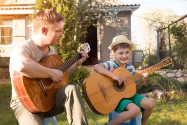 Mutlu aile babası ve çocuğu müzik aletleriyle eğleniyor açık havada gitar çalıyorlar. Baba oğluna gitar çalmayı öğretiyor. Karantinaya alındı. müzik konsepti