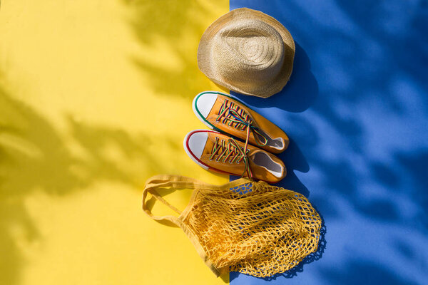 mesh shopping bag, straw hat and  Yellow sneakers on yellow background with shadows of trees. End of quarantine. Hello summer. summertime