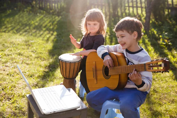 Mutlu çocuklar, erkek ve kız kardeşler dışarıda müzik aletleriyle eğleniyorlar. Gitar çalan ve pratik yaparken online dersler izleyen çocuk. Karantina.