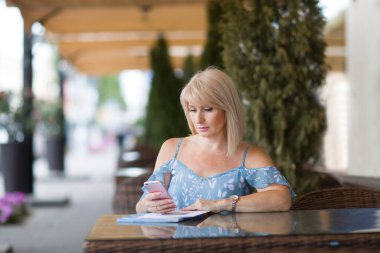 Sarışın, orta yaşlı bir kadın yaz günü açık hava kafeteryasında. seyahat kavramı