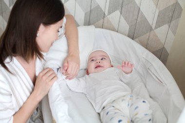 Beşikte yatan küçük bir bebek ve genç anne onun etrafında oturuyor. Mutlu aile.