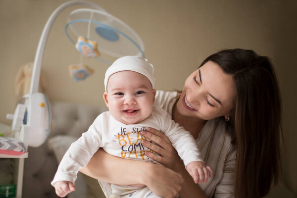happy smiling young mother playing with her with newborn baby in the bedroom. parenthood concept
