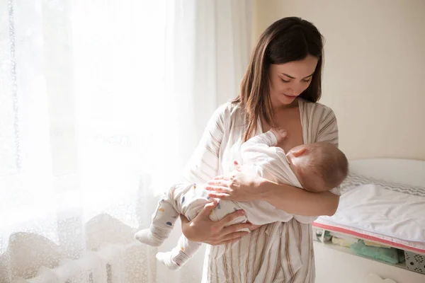 Mutlu gülümseyen genç anne yeni doğmuş bebekle yatak odasında oynuyor. Ebeveynlik kavramı
