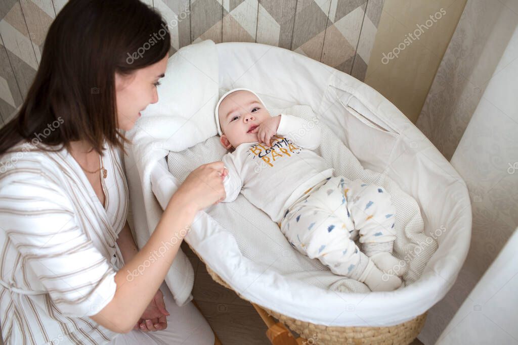 Little baby lying in crib and young mother sits about it. happy family.