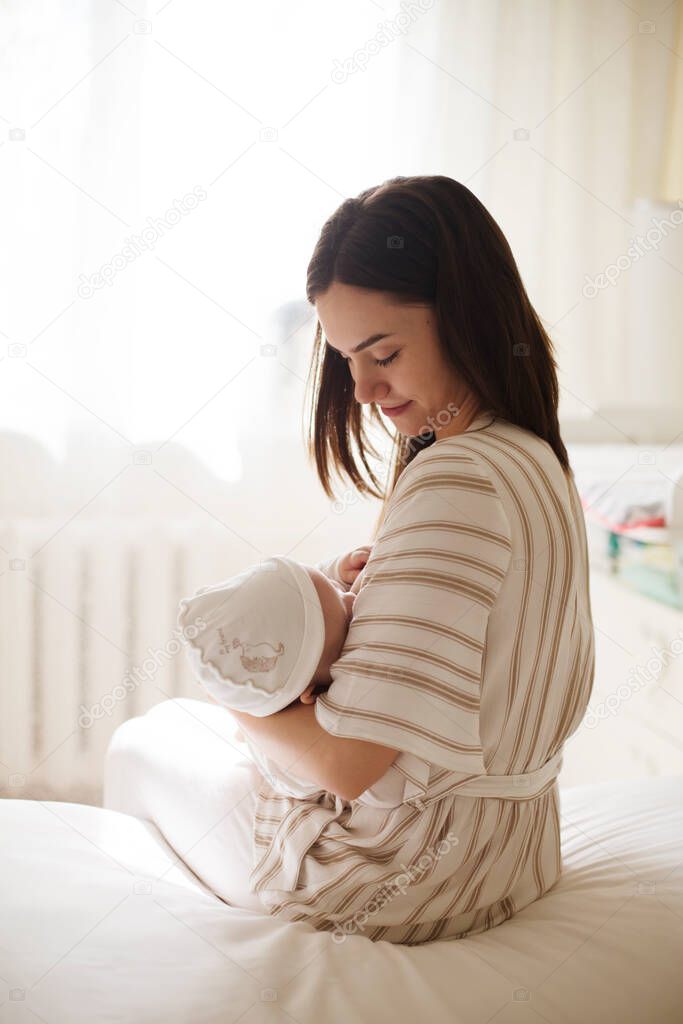 happy smiling young mother playing with her with newborn baby in the bedroom. parenthood concept