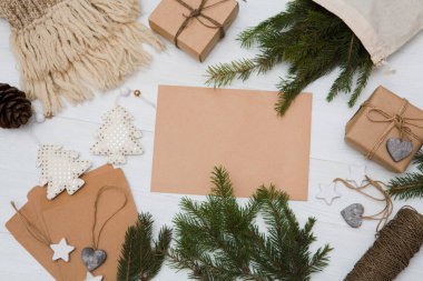 Sıfır atık, çevre dostu Noel, el yapımı hediyeler, doğal Noel süslemeleri, yün atkı, ahşap bir masada çam dalları. Düz yatış, üst görünüm, beyaz kağıt üzerinde yazı. El yapımı Noel hediyeleri