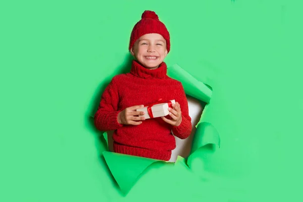 Szczęśliwe Dziecko Czerwonym Swetrze Kapelusz Prezentem Rękach Pozuje Przez Dziurę — Zdjęcie stockowe